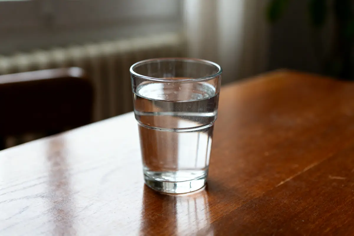 Verre d'eau de 50 centilitros posé sur une table en bois éclairée par la lumière